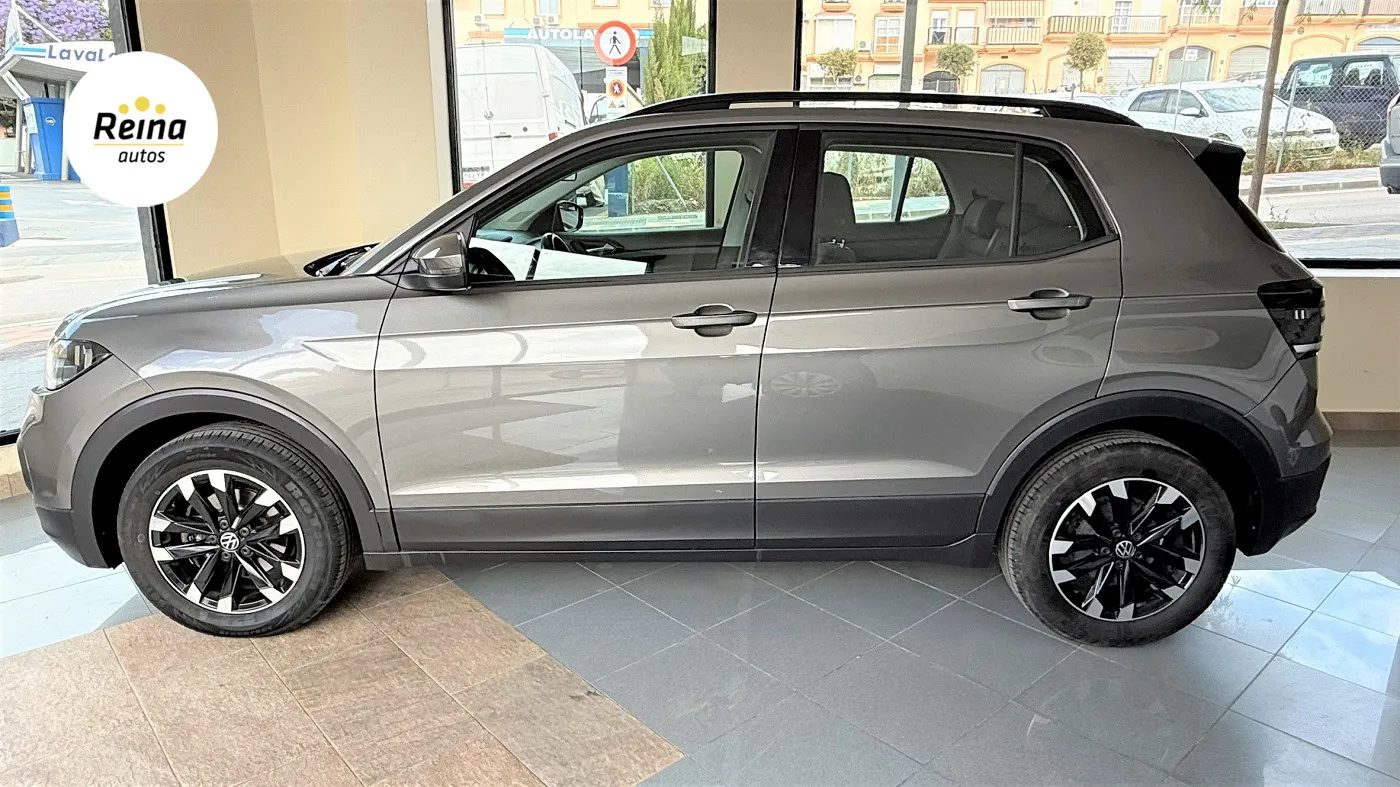 Vista lateral del Volkswagen T-Cross gris con barras de techo y llantas bicolor